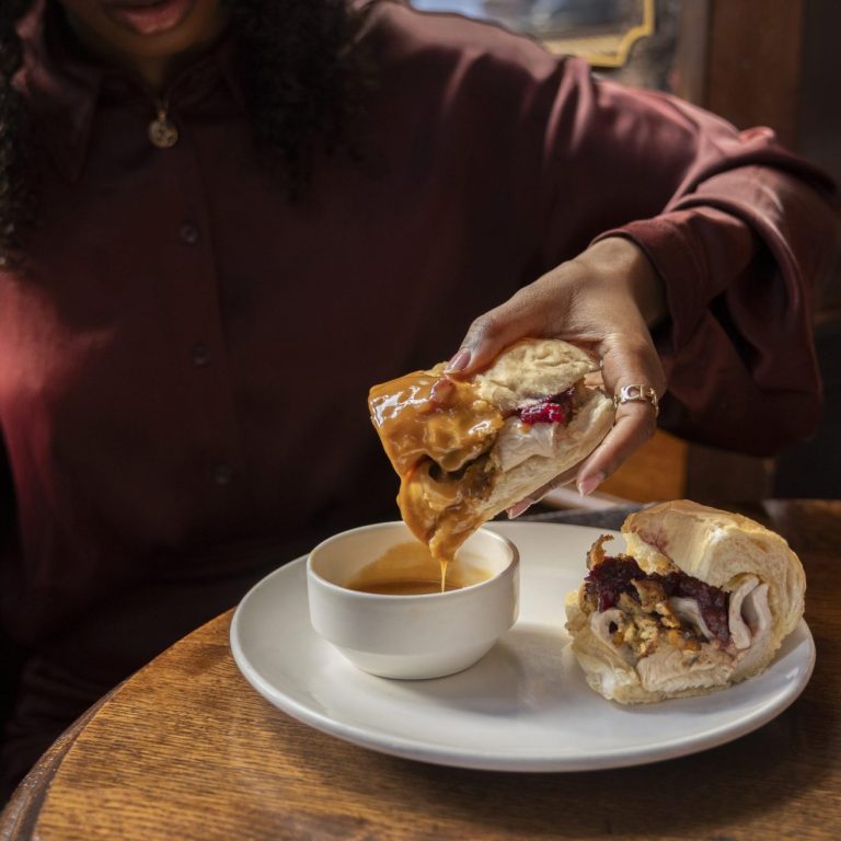 A sandwich being dipped into gravy. A festive twist on our popular London Dip sandwich, with turkey, stuffing and Farm Shop cranberry sauce.