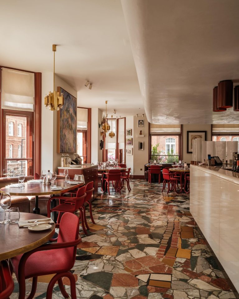 An interior view of Mount St. Restaurant – palladium marble flooring with leather-top circular red tables and red chairs. Artwork on the walls in the background.